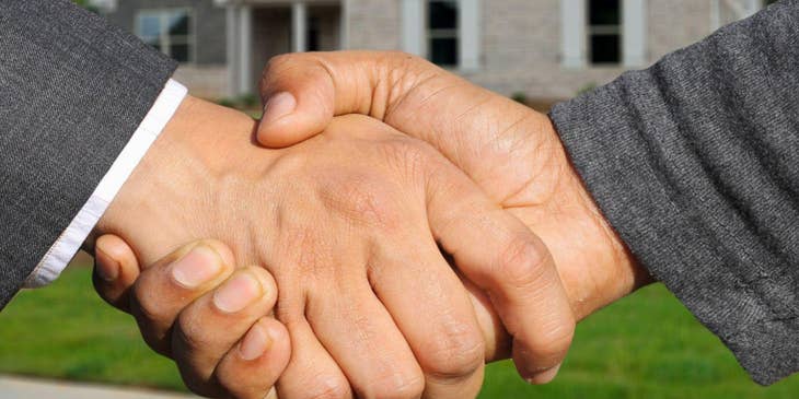Un agente contratado por una bolsa de trabajo de bienes raíces dándole la mano a un cliente frente a una casa.
