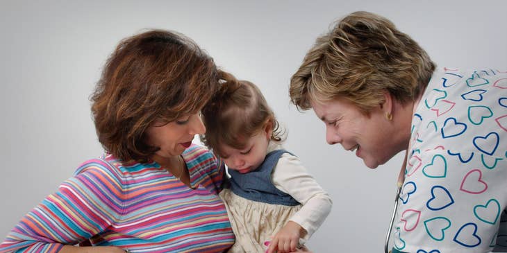 Pediatric medical assistant gives vaccine shot on the leg as the patient's mother comforts her