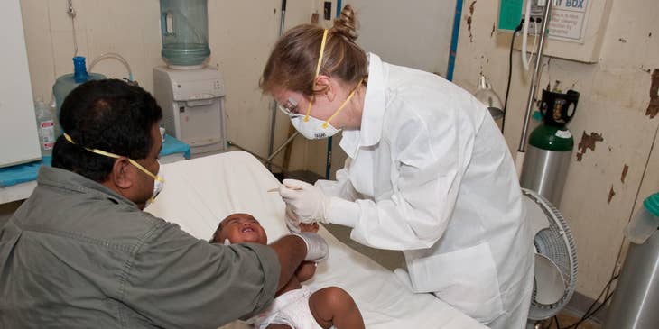 Pediatrician prepares to check  the infant's mouth using a depressor while the baby is lying down