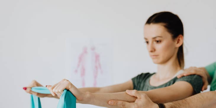 Physical therapist assistant guides the patient in muscle stretching using an elastic band