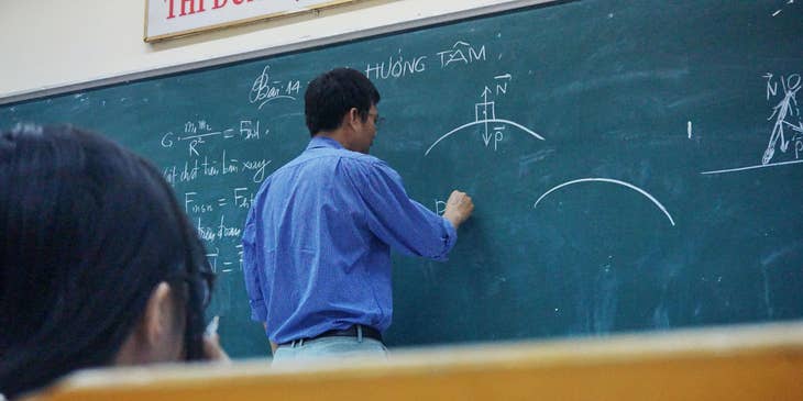 Physics teacher explaining the formula to students while writing on the board