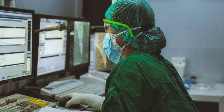 Practice manager in full PPE working on a desktop.