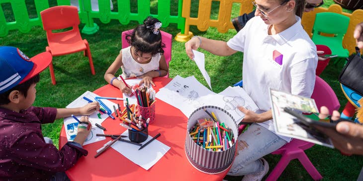 Preschool director overseeing outdoor activities while checking student's artwork