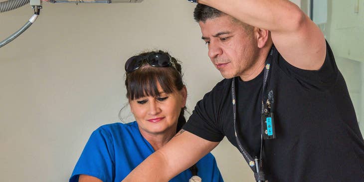 Radiology Technician shows how to properly position the hand in an Xray machine to a colleague