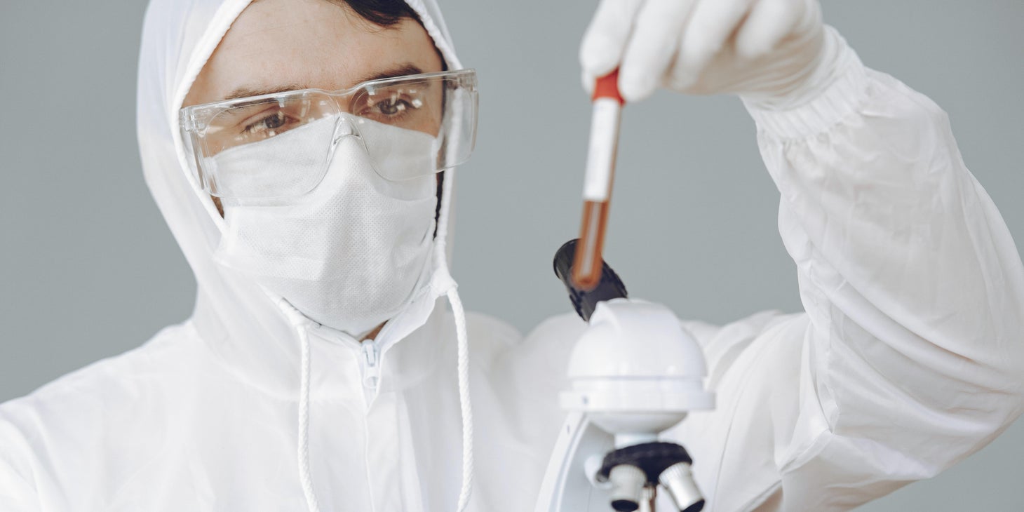 Virologist examines a blood sample under a microscope to check for viruses in a protective suit