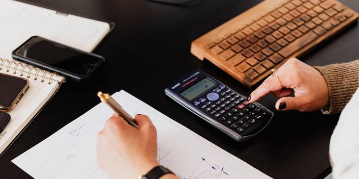 Accountant using calculator and taking notes on paper.