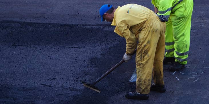 Asphalt Laborers smoothing and setting asphalt on the road.