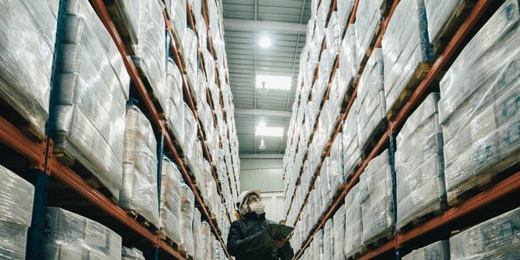 Automated Logistical Specialist in holding a clip board in a warehouse doing inventory of stocks.