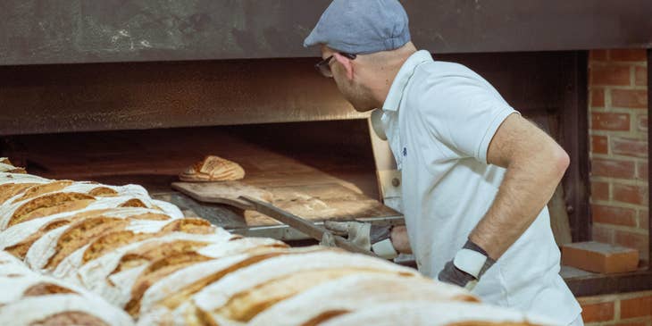 Baker taking out a freshly baked bread out of the oven.
