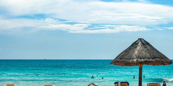 Vista de unos camastros, palapa y el mar de fondo en Cancún.