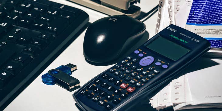 A scientific calculator alongside a keyboard, mouse, stapler, and paperwork.