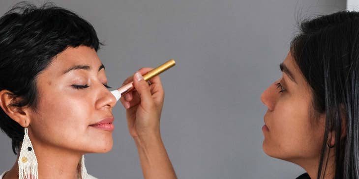 A makeup artist applying blush to their client's face.