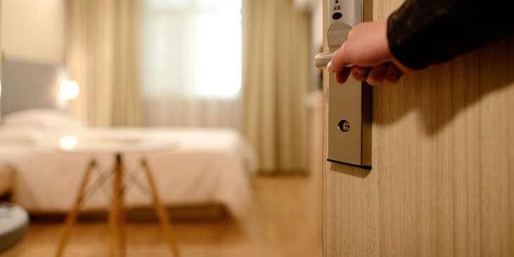 A hospitality professional opening a hotel room door.