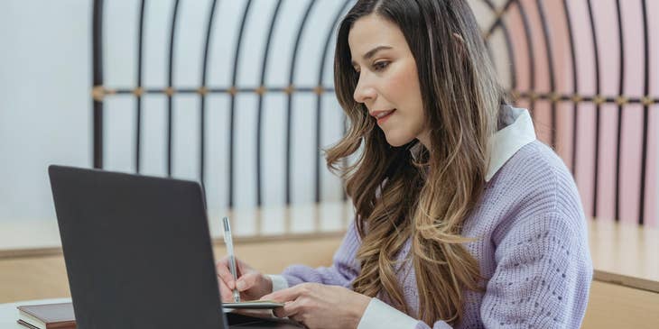 A clinical case manager looking at their laptop and writing in a notebook.