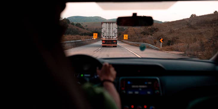 Conductor de camión sosteniendo el volante de su trailer con la vista trasera de un transporte de carga frente a él.