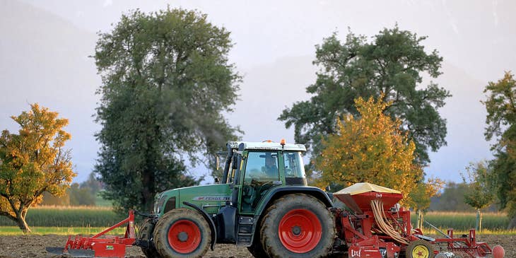 Una granja con tractor y otros equipos agrícolas con un empleado contratado por una bolsa de trabajo para agricultura.