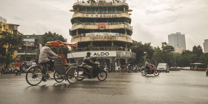 Hanoi street with mopeds, cars and cyclists driving past in Vietnam.