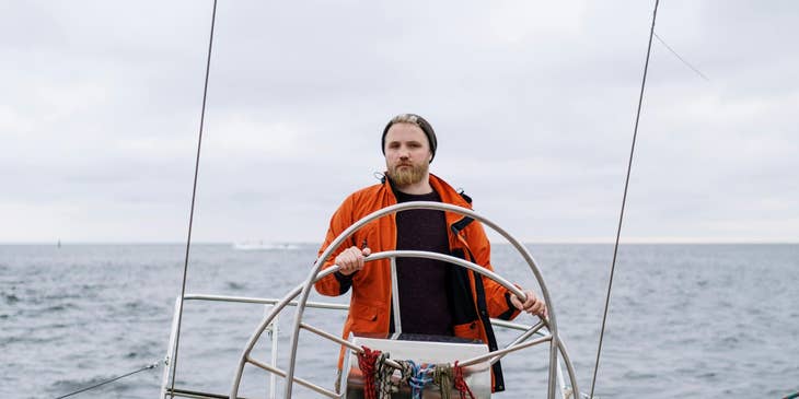 Maritime captain steering a sailboat.