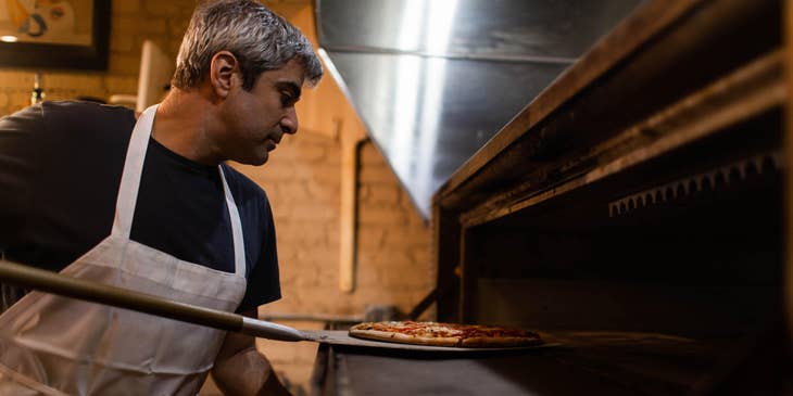 A pizza maker putting a pizza into an oven.