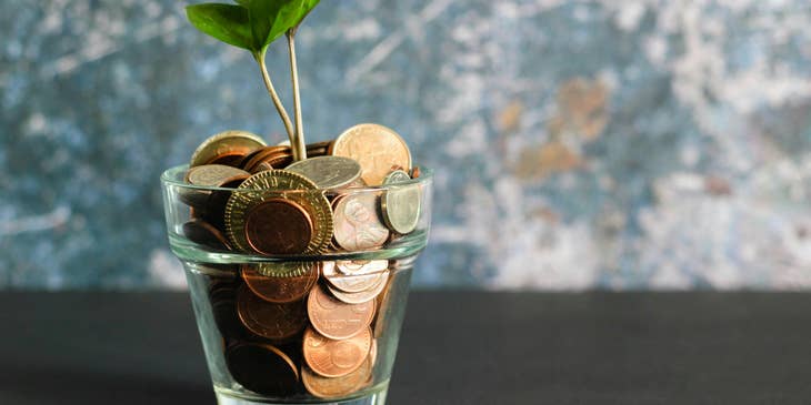 Una maceta de vidrio con monedas de oro de las cuales florece una planta.