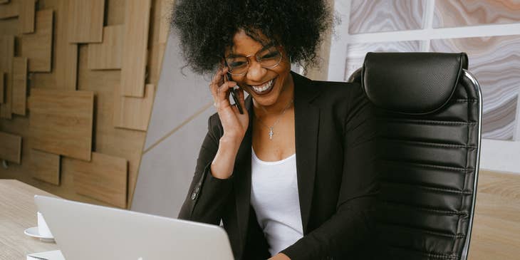 Una sonriente mujer atendiendo una llamada telefónica después de enviar un correo electrónico anunciando al nuevo integrante del personal.