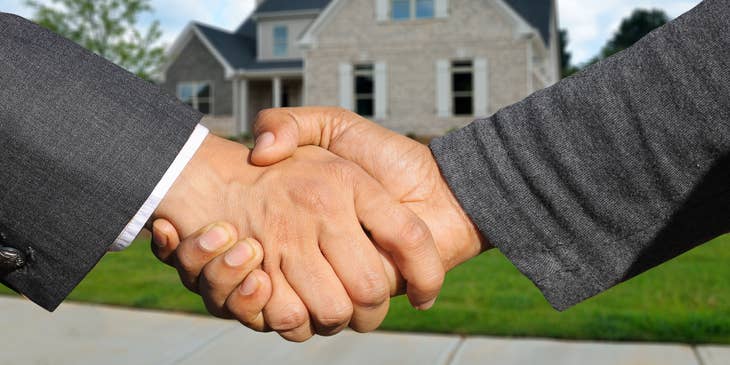 Two people shaking hands on a real estate deal in front of a house.