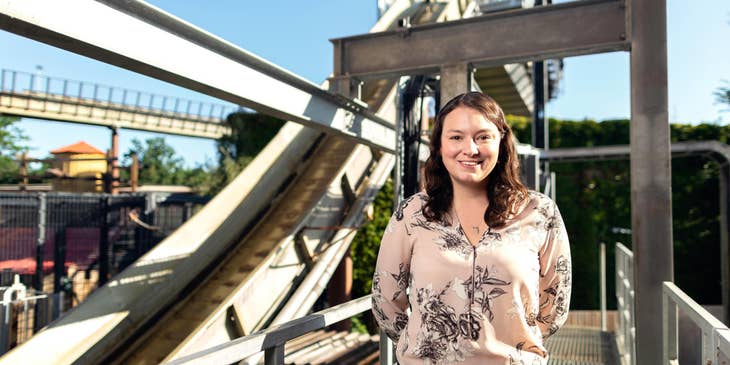 A recreation attendant standing in front of a rollercoaster in an amusement park.