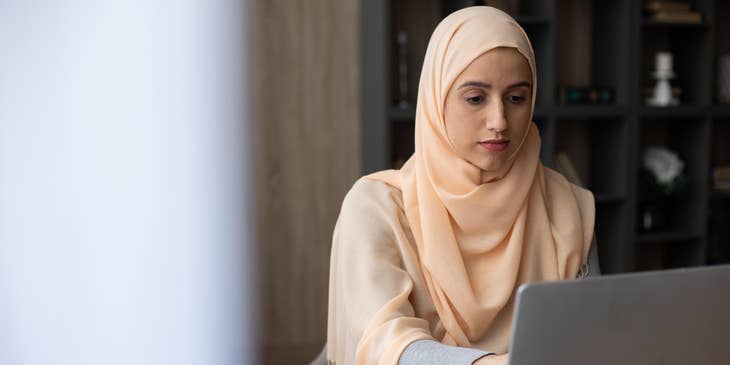 A social media representative working on a laptop with a notebook on the table.