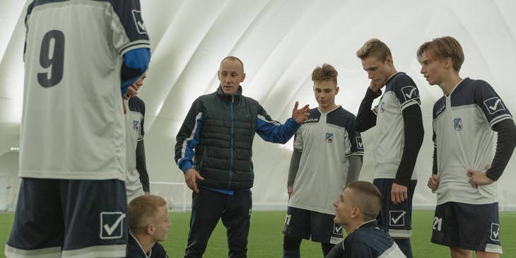 Sports coach talking to a team of soccer players in an indoor field.