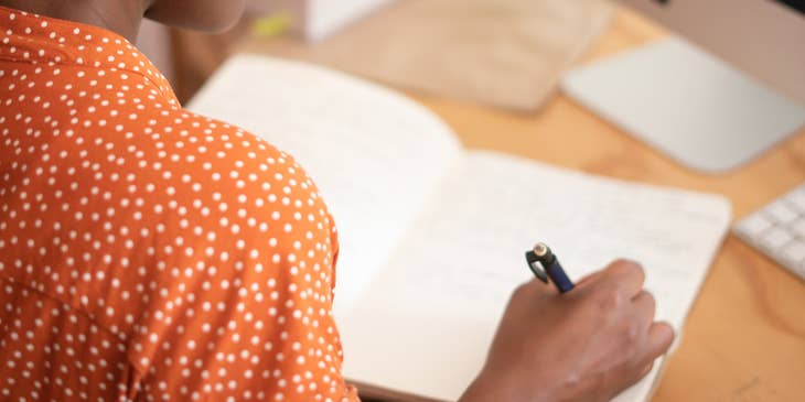 A transition manager writing in a notebook at a desk with a computer.