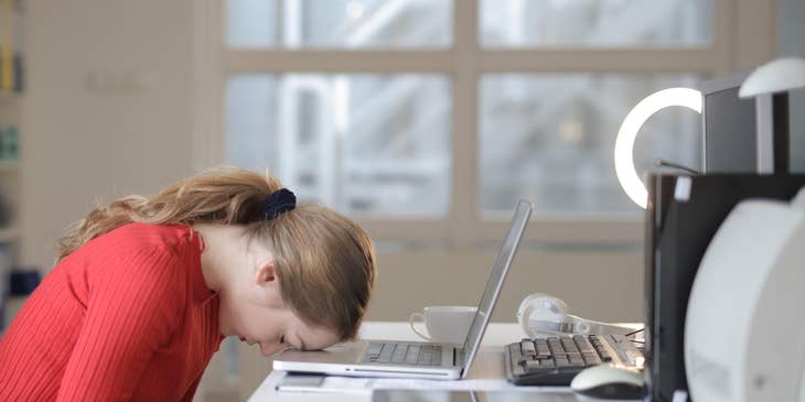 employee in red and black resting forehead on laptop