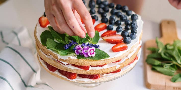 Cake Decorator decorating a cake with fruits and mint