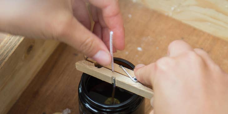 A Candle Maker dipping and preparing candle wicks inside the glass molds filled with molten wax.