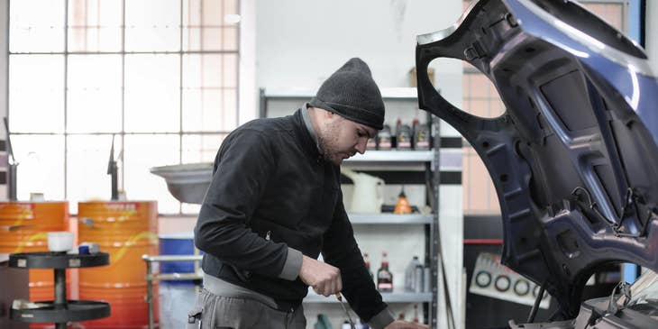 A Car Porter in an automotive workshop holding a dip stick to ensure oil is sufficient or needs to be refilled.