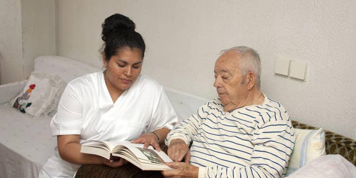 The carer assist an elderly in reading books.