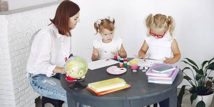 Childcare Worker looking after two girls painting at the table