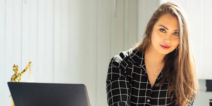 Compliance Engineer sitting on her workstation with an open laptop and signing papers on her desk