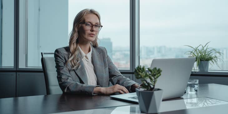 Credit Manager wearing a gray blazer and sitting on an office desk while looking at her laptop