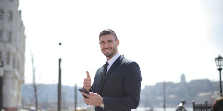 Customer Success Manager smiling and wearing a business suit while giving a thumbs up and holding his mobile phone