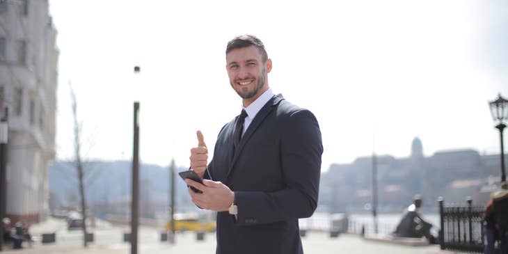 Customer Success Manager smiling and wearing a business suit while giving a thumbs up and holding his mobile phone