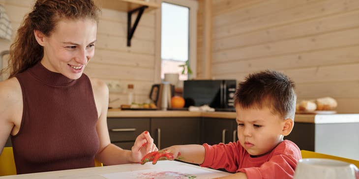 Day Care Director oversees child development as the toddler plays hand painting on a paper