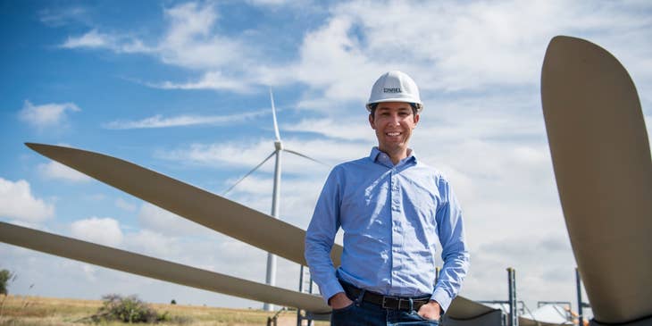 Environmental Engineer wearing a hard hat while standing along the line of wind turbines