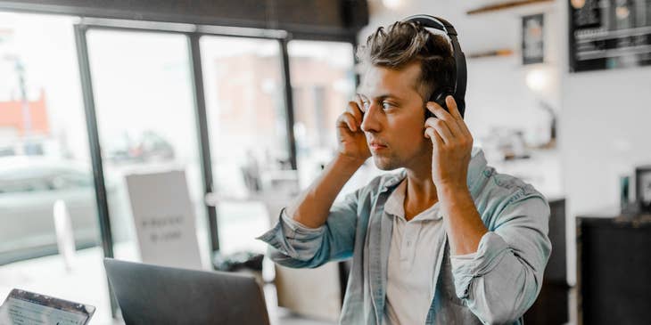 male Financial Services Representative sitting with his laptop open on a desk while fixing his headset