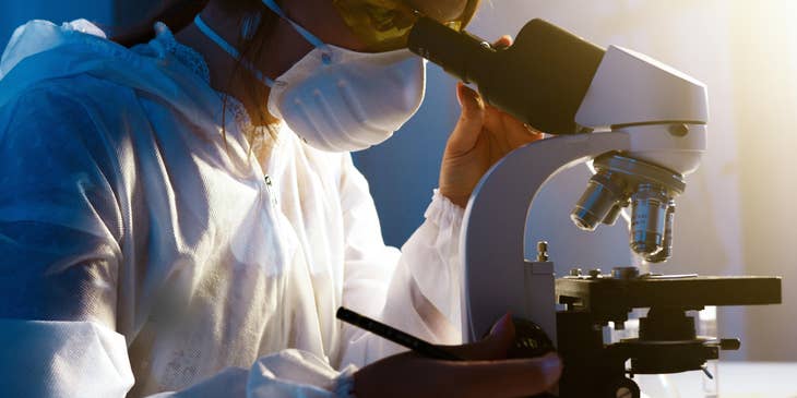 A Female Forensic Scientist in a laboratory interpreting evidence collected from a crime scene through a microscope.