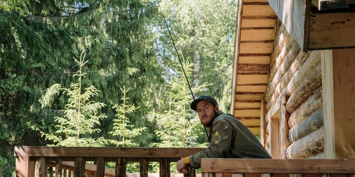 Forest Ranger leaning from the railings of the log cabin in the middle of the forest