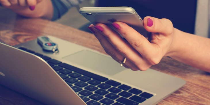 Close-up of a front-end developer's hands holding a cellphone behind a laptop