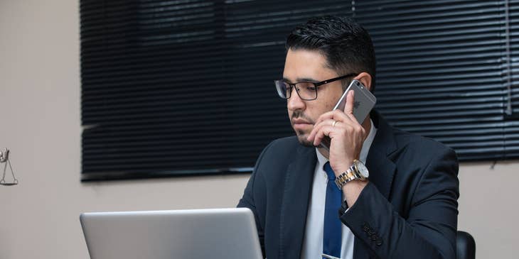 A General Counsel in his office in front of his laptop working on some legal documents while talking on the phone.