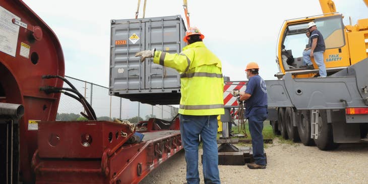 The Heavy Equipment Operator maneuvers the machine to transfer a container.