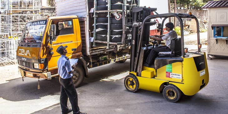 An Industrial Truck and Tractor Operator driving a tractor loading tires and about to transport items inside the warehouse.