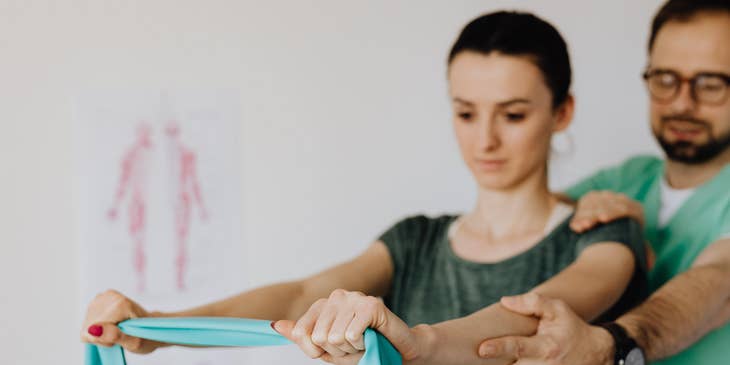 Kinesiologist monitoring patient muscle movements while using an elastic band.